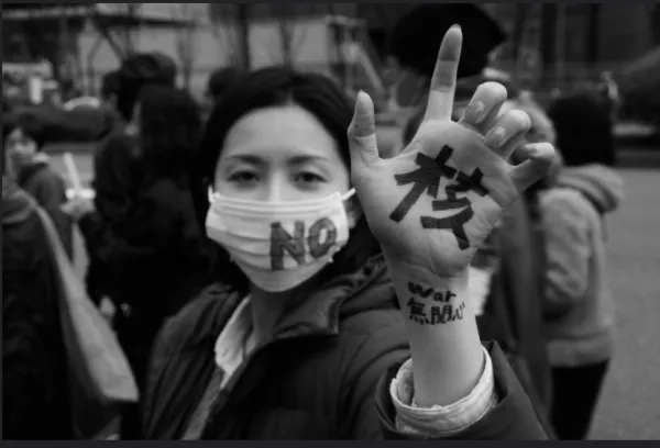 Young Japanese woman with mask on that says No and her hand says Nukes in Japanese