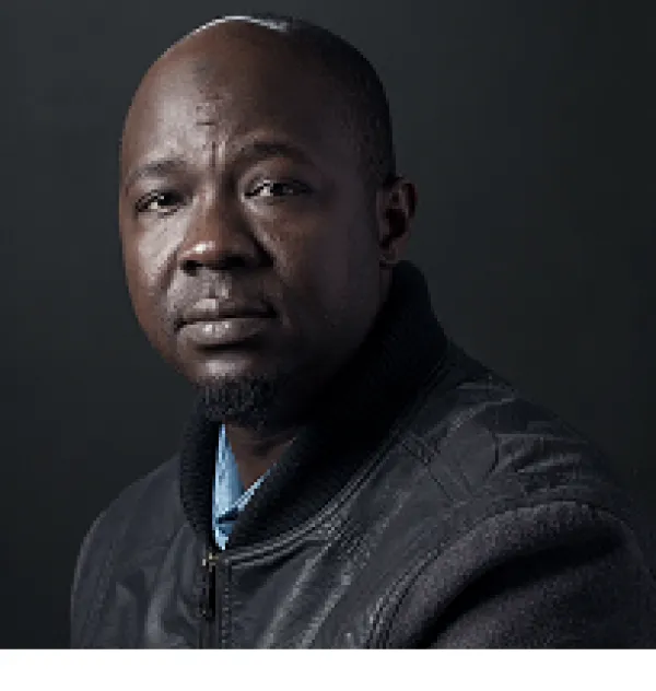 Middle aged black man, bald, in grey sweater, looking at the camera like he's a bit sad and a bit let down