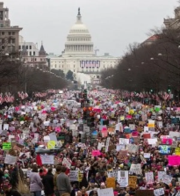 Building with round white  dome, tree lined street, lots of protestors wearing pink