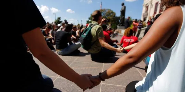 People sitting on ground holding hands and women in foreground holding someone's hand