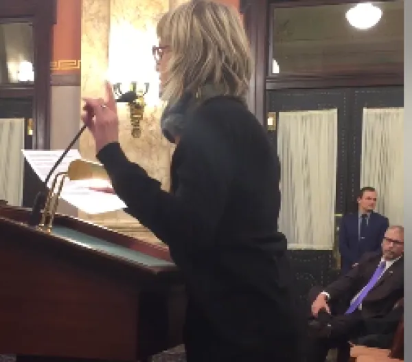 White woman with short blonde hair taking animatedly at a podium