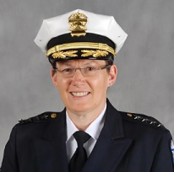 White woman in wire-rimmed glasses smiling in a pose with a police hat and uniform on