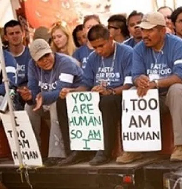 Latino men wearing blue shirts sitting and holding signs that say I Too, Am Human
