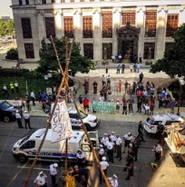 Scene in downtown with tall office buildings lots of people in the streets with protest signs, a lot of police and a tepee looking wooden structure