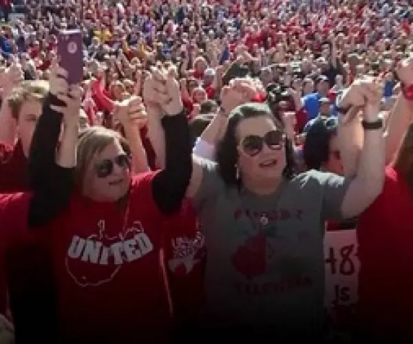 Lots of people in the background and in the foreground two heavyset middle aged ladies holding hands with arms above their heads in victory pose