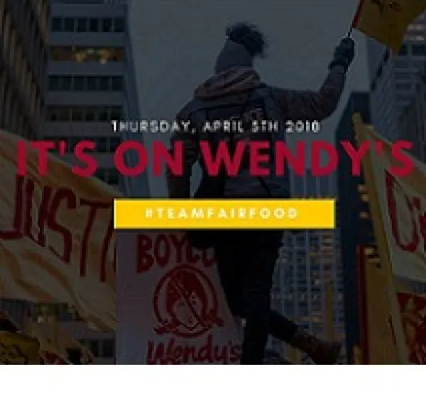 Darkened photo of back of a black woman outside waving a yellow flag over her head and signs all around her about justice and against Wendys