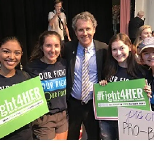 Three young women with #Fight4HER signs and one older white man in a suit