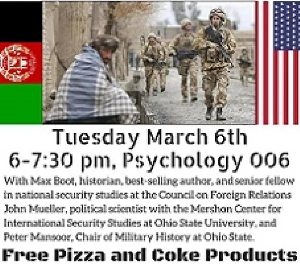 Photo of men in combat fatigues holding automatic weapons walking through a village of civilians who look very poor