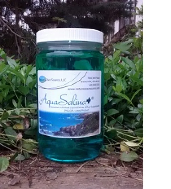 Glass looking bottle with white lid and label that says AquaSalina sitting outside in nature with grass and trees around