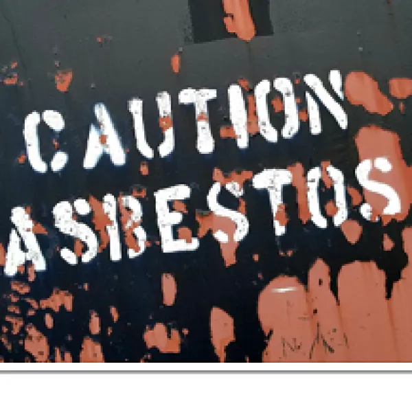 Black and pick mess on a floor and words Caution Asbestos