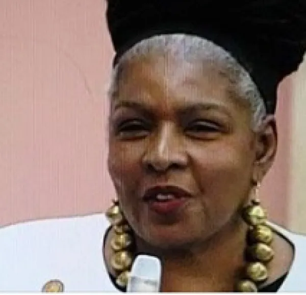 Black woman with A large gold necklace talking into a mic