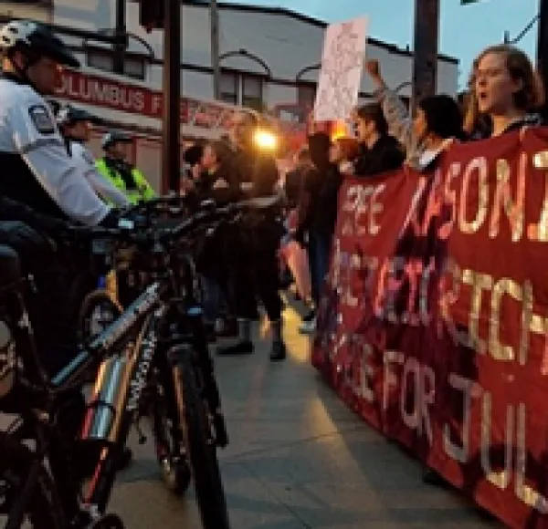 Police on bikes facing off at a banner held by people saying Free Masonique