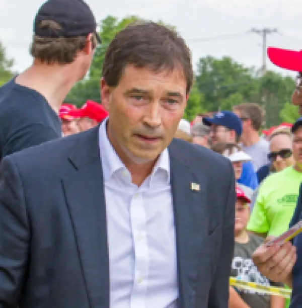 MIddle aged white man in a white button down shirt under a blue sportcoat outside with a confused look on his face
