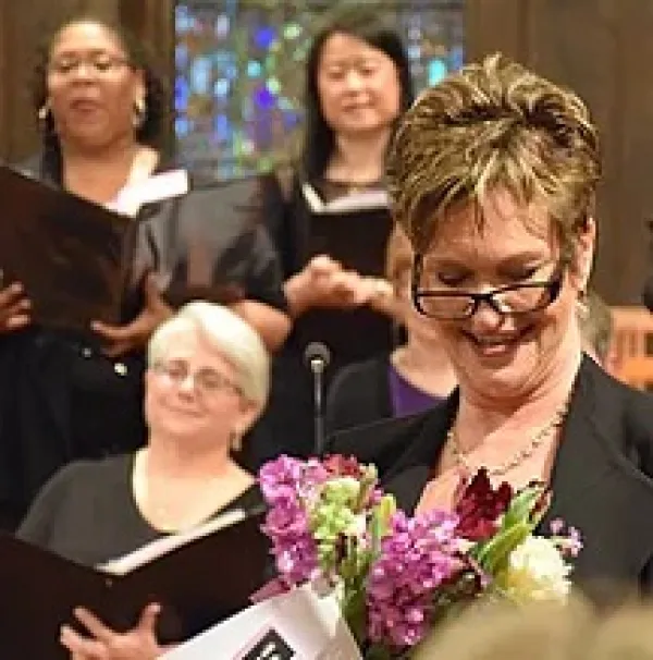 Three women in background holding songbooks and one in foreground smiling and holding flowers