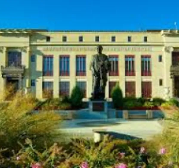 Big white government building with tall gray statue out front and some greenery in the foreground
