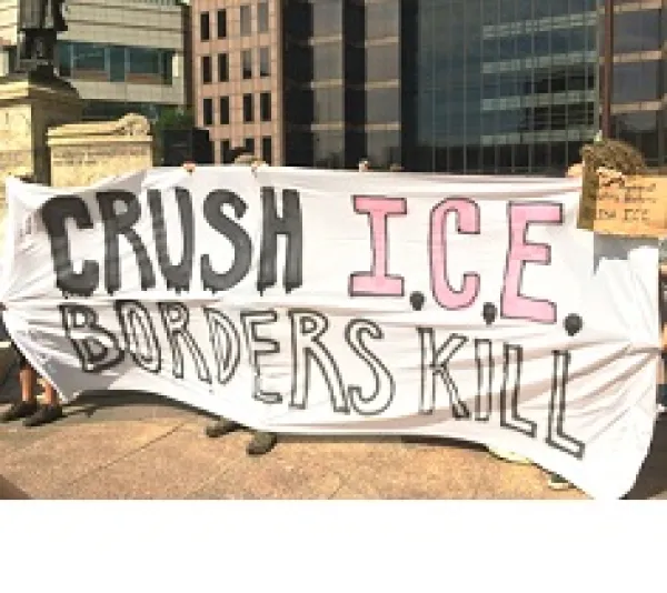 People at rally holding banner reading Crush ICE borders kill