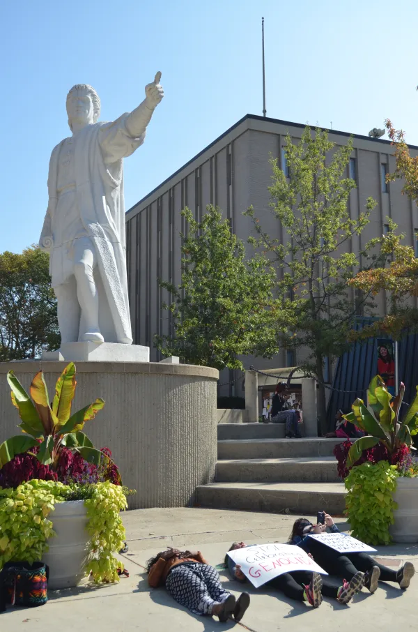 Student lying on ground beneath Columbus statue