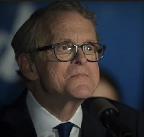 Older white man with glasses looking weird and crazy in a suit at a microphone
