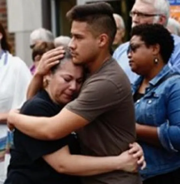 Young man hugging a shorter older woman with other people looking on in the background