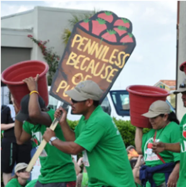 People of color in green shirts marching and holding signs one that says Penniless 