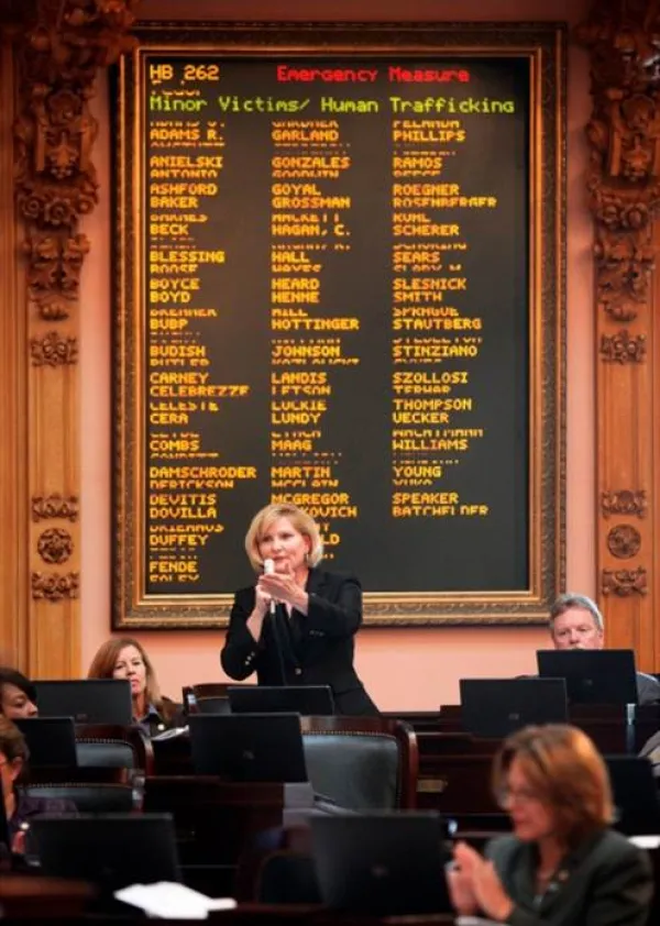 Blonde woman speaking to a crowd in front of a sign with names of people who were victims of human trafficking