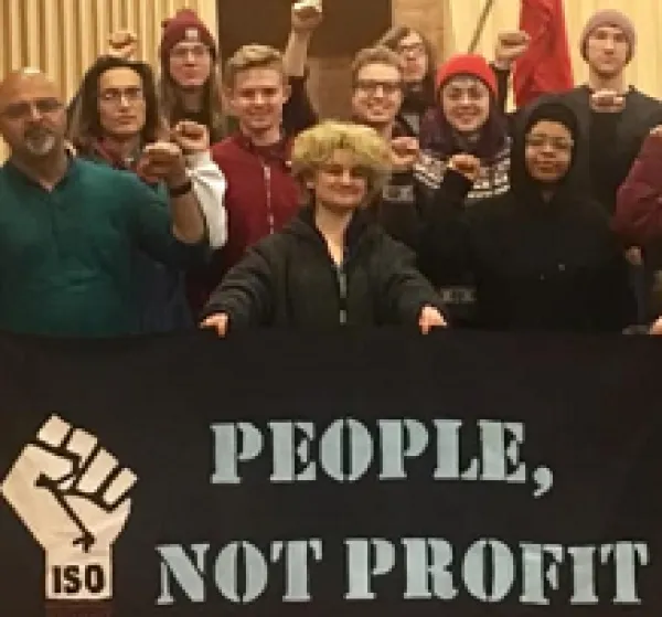 Lots of people posing holding a sign with a fist and words People. Not Profits