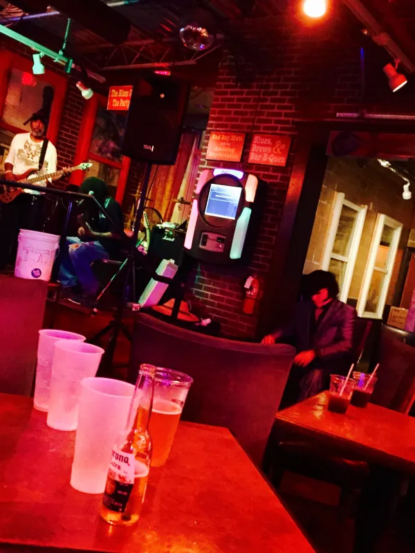 Sideways view of a bar with guy with guitar on stage lighting is very red