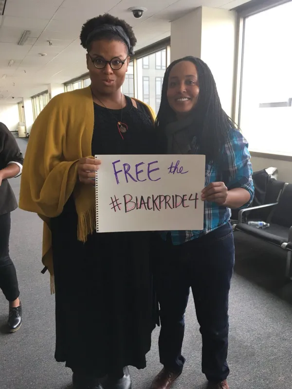 Two people with photo cutting off their heads holding a sign that says Free the Black Pride 4
