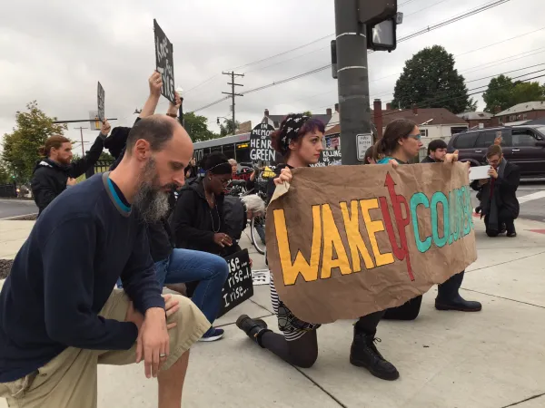 Protesters with signs down on one knee
