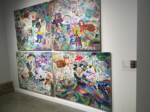 Paintings hanging on a white wall that are very large one on top of the other and of very colorful scenes
