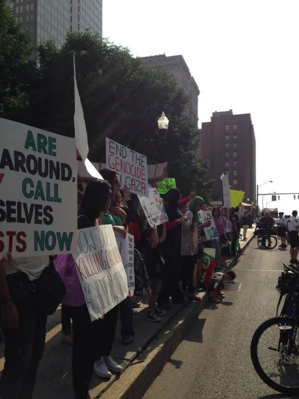 View down a sidewalk with people holding signs demonstrating and some bike cops facing them