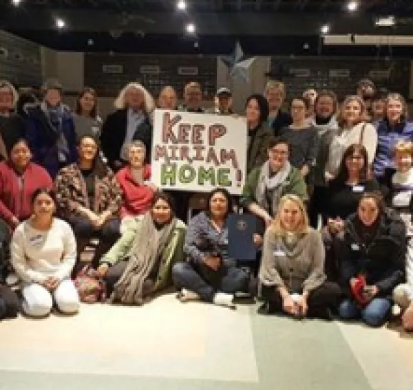 Lots of people in rows posing for the camera holding a sign that says Keep Miriam Home