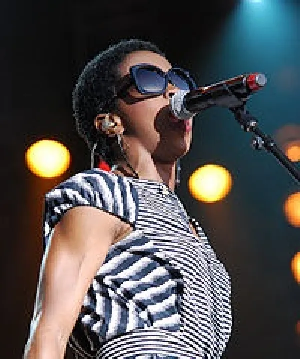 Black woman wearing sunglasses and a striped dress singing into a mic
