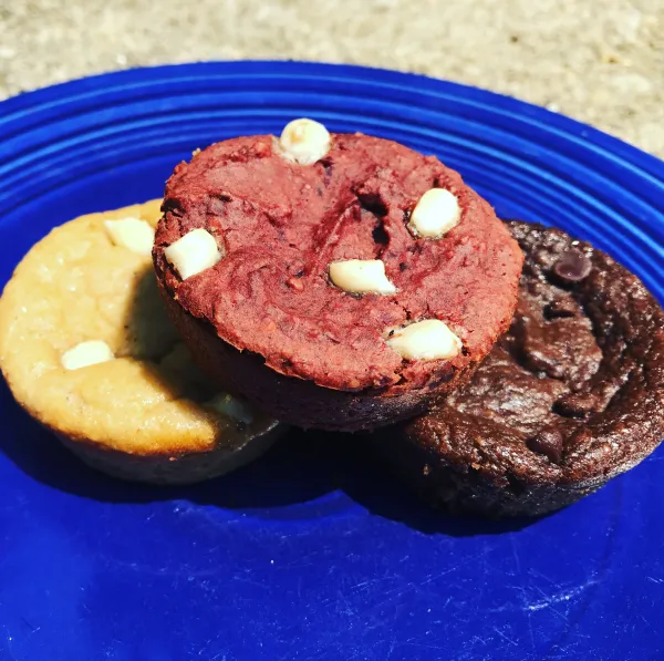 Cupcake-looking desserts, round, each one a different color, yellow, brown and dark brown with white chocolate chips on a blue plate