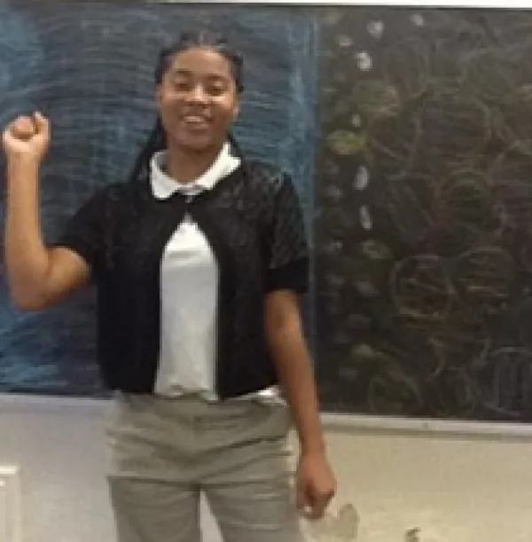 Young black woman standing in front of a blackboard with a smile and raising her right hand