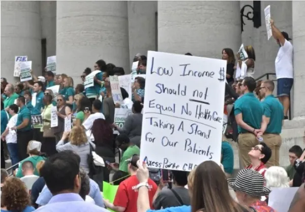 Person holding a sign against the Medicaid cuts at the statehouse with lots of other people