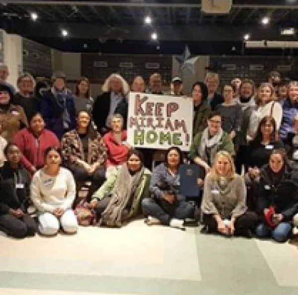 Lots of people in rows posing for the camera holding a sign that says Keep Miriam Home