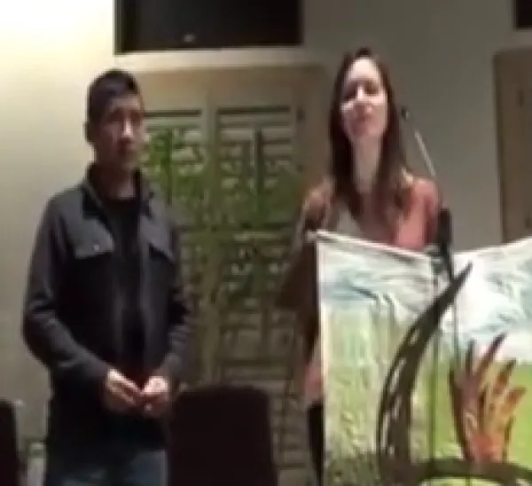 Latino man and white woman standing at front of event speaking
