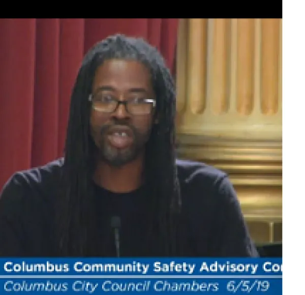 Black man in dreads talking at a mic