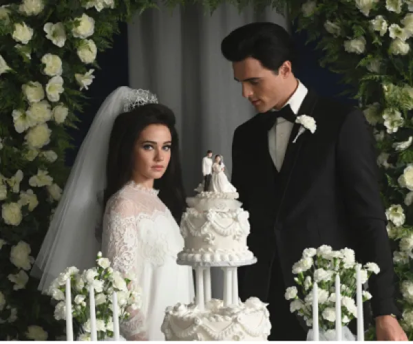Priscilla and Elvis at wedding in front of wedding cake
