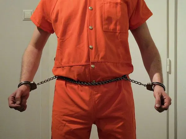 Guy in orange jumpsuit and chain around his belly attached to his wrists