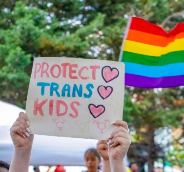 Someone holds aloft a sign reading "Protect trans kids." 
