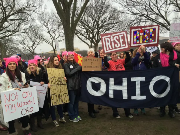 Women outside wearing pink winter hats holding signs and a big banner that says OHIO