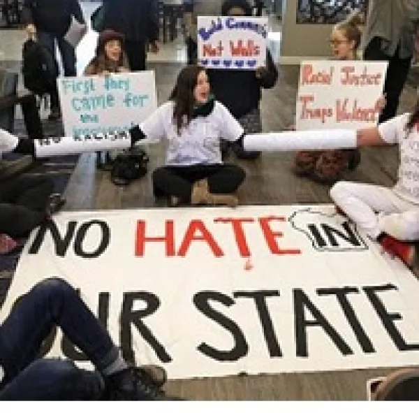 People sitting in a circle on the ground with signs, one in the middle says No hate in our state