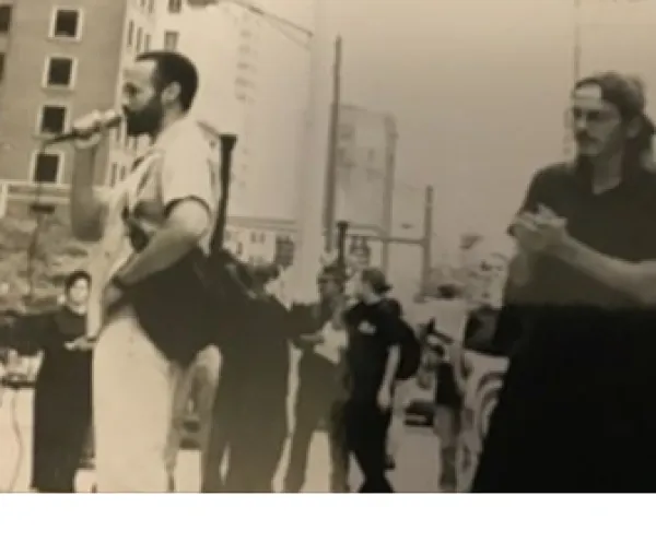 Black and white grainy photo of black man speaking at a mic and people protesting on a street