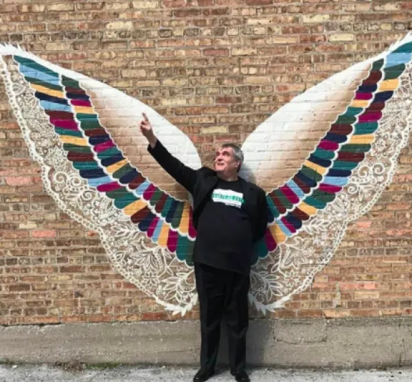Man standing in front of an art piece of two big wings against a wall