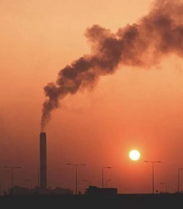 Orange sky with prominent smokestack spewing smoke and sun barely peeking through