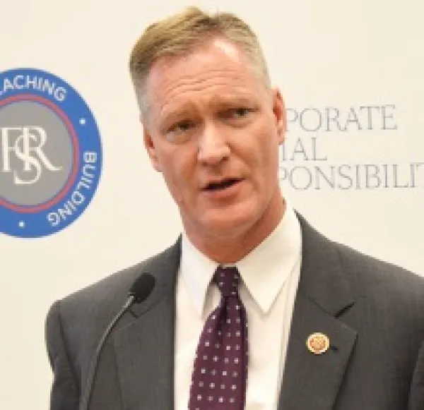Thin white man in a suit speaking at a mic