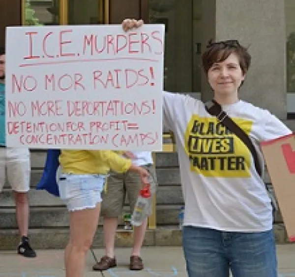 White woman in Black Lives Matter Tshirt holding a sign that says ICE murders