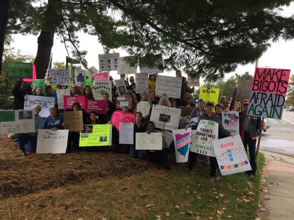A bunch of people holding signs and facing the camera posing under a tree